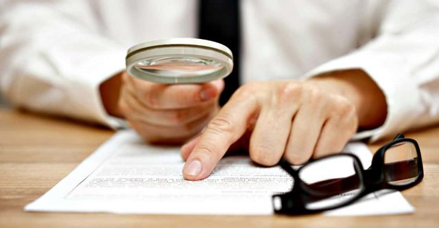 Focused businessman is reading through magnifying glass document